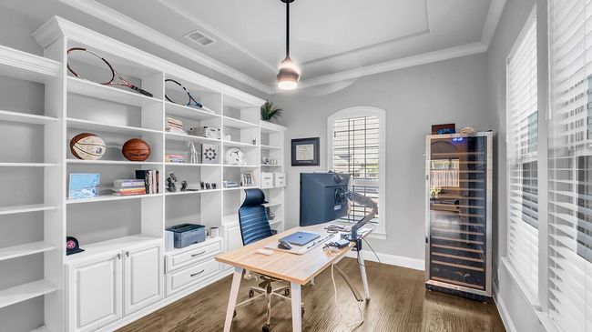 Office area featuring dark wood finished floors, crown molding, visible vents, ceiling fan, and beverage cooler | Image 13