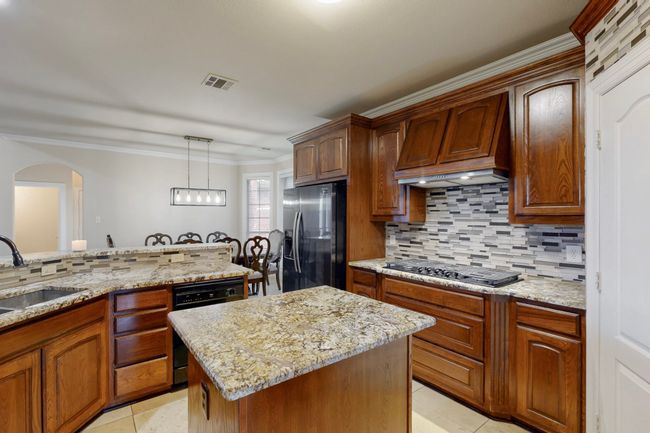 Kitchen with visible vents, stovetop with downdraft, a sink, stainless steel fridge, and custom range hood | Image 11