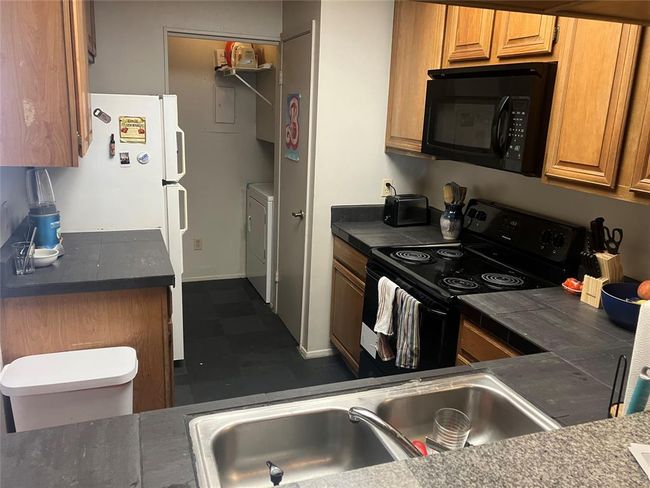 Kitchen featuring black appliances, a sink, washer / clothes dryer, dark floors, and dark countertops | Image 6