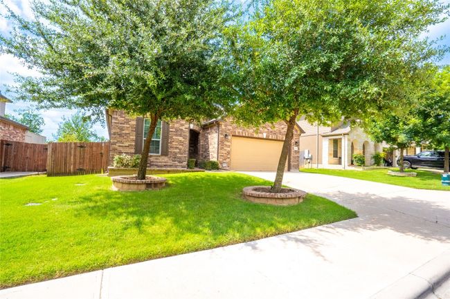 View of property hidden behind natural elements with driveway, brick siding, an attached garage, and a gate | Image 33