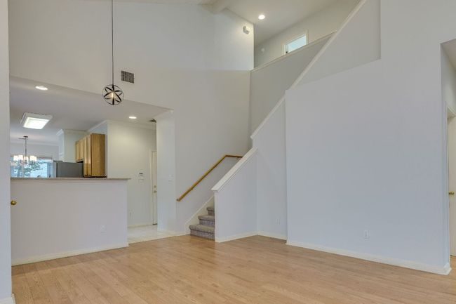 Unfurnished living room with a chandelier, stairs, a high ceiling, light wood-style flooring, and recessed lighting | Image 8