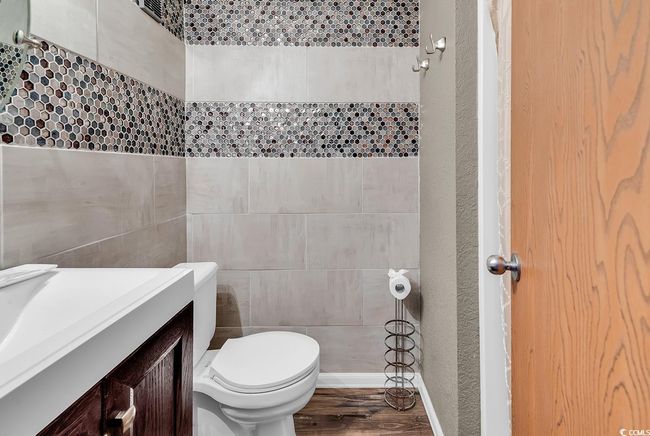 Half bathroom with tile walls, toilet, wood finished floors, vanity, and a textured wall | Image 11