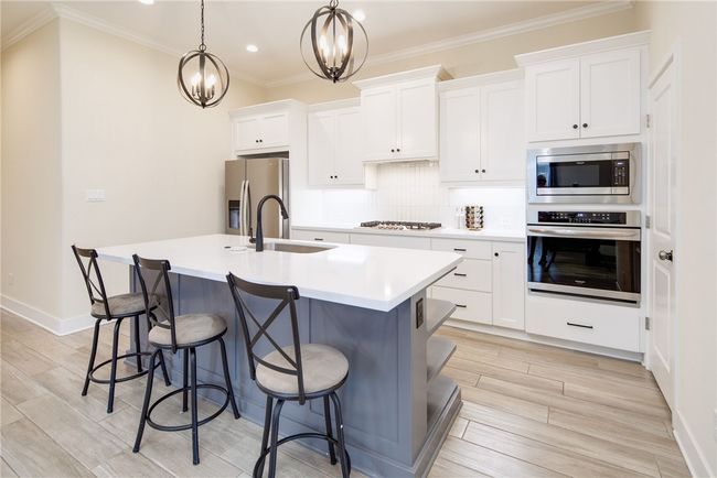 Kitchen with stainless steel appliances, a center island with sink, a kitchen breakfast bar, white cabinets, and a sink | Image 7