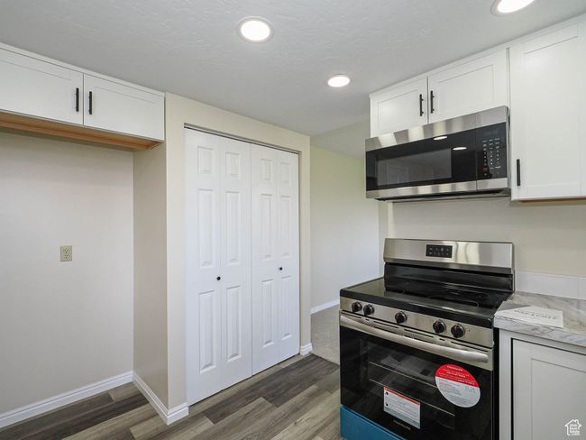 Kitchen with stainless steel appliances, dark wood-style flooring, white cabinets, recessed lighting, and light countertops | Image 32