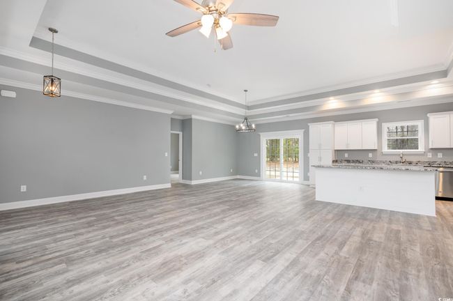 Unfurnished living room featuring ceiling fan, light wood-type flooring, ornamental molding, and a tray ceiling | Image 4