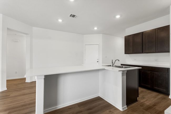 Kitchen featuring dark brown cabinets, dark wood finished floors, light countertops, recessed lighting, and an island with sink | Image 8