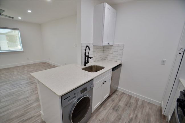 Kitchen featuring washer / clothes dryer, light wood-style floors, decorative backsplash, light stone countertops, and white cabinetry | Image 4
