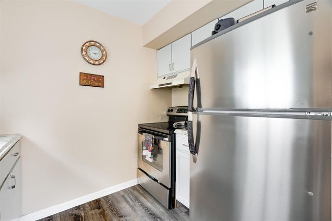 Kitchen featuring stainless steel appliances, under cabinet range hood, dark wood-style flooring, light countertops, and white cabinetry | Image 11