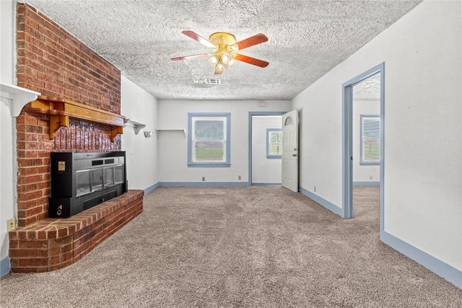 Unfurnished living room with a textured ceiling, carpet, a fireplace, and ceiling fan | Image 12