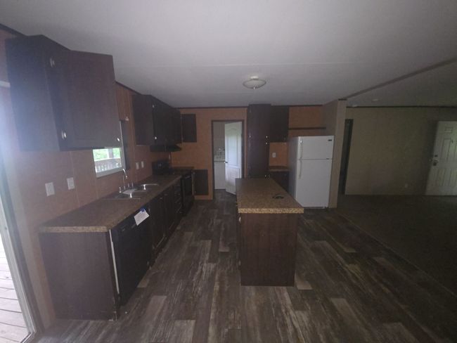Kitchen with dark wood finished floors, black appliances, a kitchen island, light countertops, and a sink | Image 7
