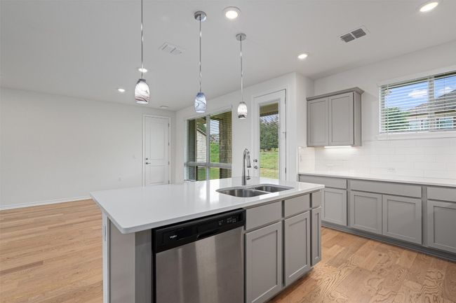 Kitchen with light wood finished floors, stainless steel dishwasher, gray cabinets, and a center prep sink | Image 8