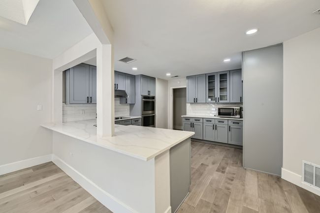 Kitchen featuring light stone countertops, stainless steel appliances, under cabinet range hood, a peninsula, and gray cabinetry | Image 8