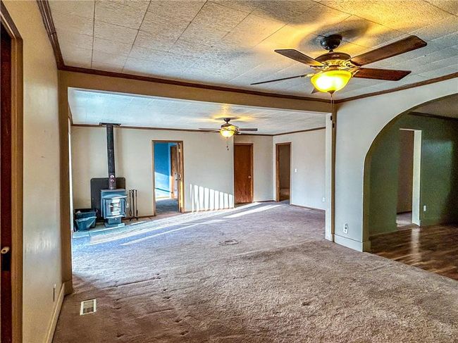 Unfurnished living room with arched walkways, crown molding, dark colored carpet, visible vents, and a wood stove | Image 7