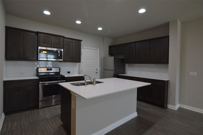 Kitchen featuring stainless steel appliances, a sink, baseboards, a center island with sink, and backsplash | Image 4