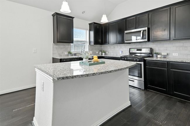 Kitchen featuring stainless steel appliances, backsplash, dark wood-type flooring, vaulted ceiling, and light stone counters | Image 13