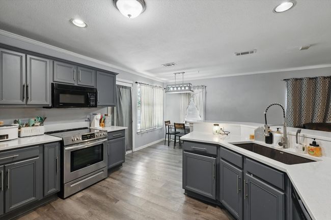 Kitchen with black microwave, stainless steel electric range, crown molding, gray cabinets, and light countertops | Image 14