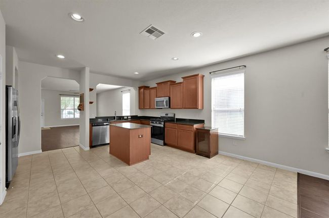 Light tile flooring, plenty of natural light from a large window, and warm wood cabinetry. It includes modern stainless steel appliances, a central island, and ample counter space, perfect for cooking and entertaining. | Image 11