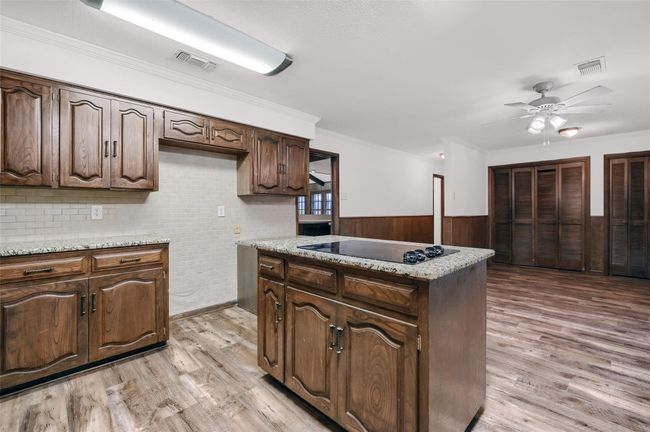 Kitchen with light wood-style flooring, a ceiling fan, wainscoting, black electric cooktop, and wood walls | Image 9