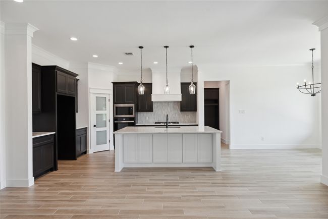 Kitchen with appliances with stainless steel finishes, pendant lighting, backsplash, a center island with sink, and light hardwood / wood-style flooring | Image 11