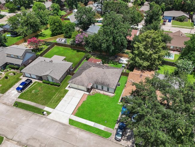 This aerial view showcases a single-story home with a spacious backyard, well-maintained lawn, and a paved driveway. The neighborhood is lush with trees, providing a serene and green environment. Nearby homes are similar in style, indicating a cohesive community setting. | Image 27