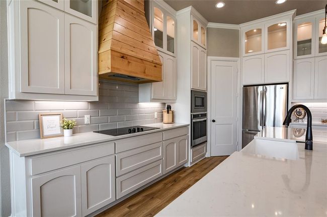 Kitchen featuring light stone countertops, stainless steel appliances, white cabinets, tasteful backsplash, and custom exhaust hood | Image 6