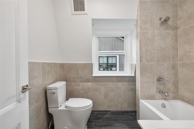 Bathroom featuring visible vents, toilet, tile walls, shower / bathing tub combination, and a wainscoted wall | Image 17