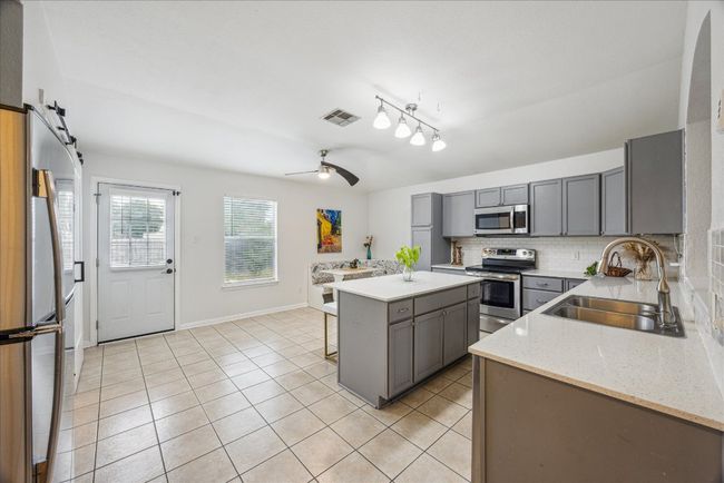 Kitchen with stainless steel appliances, gray cabinets, and light tile patterned floors, and large kitchen island | Image 7