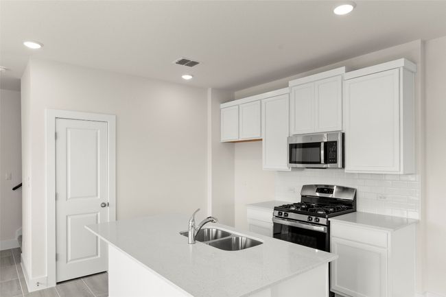 Kitchen featuring decorative backsplash, a center island with sink, white cabinetry, a sink, and stainless steel appliances | Image 17