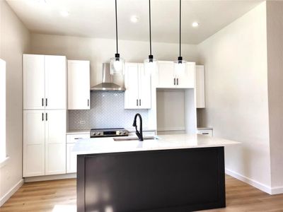 Kitchen with light hardwood / wood-style floors, backsplash, a center island with sink, and wall chimney range hood | Image 3