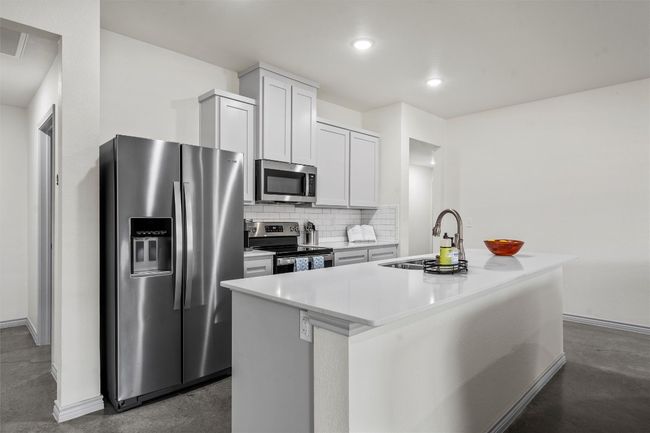 Kitchen with concrete floors, tasteful backsplash, a sink, a center island with sink, and appliances with stainless steel finishes | Image 6