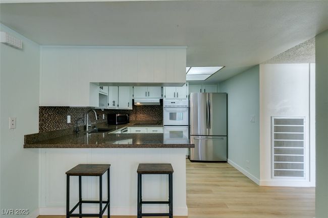 Kitchen with appliances with stainless steel finishes, a peninsula, decorative backsplash, light wood finished floors, and under cabinet range hood | Image 22