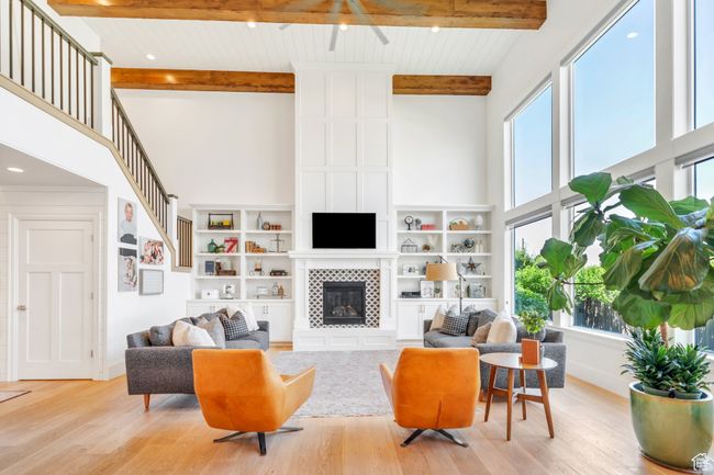 Living area featuring a towering ceiling, plenty of natural light, light wood-style floors, beam ceiling, and a tiled fireplace | Image 10