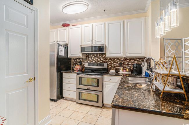 Kitchen featuring stainless steel appliances, white cabinets, light tile patterned flooring, decorative backsplash, and crown molding | Image 10