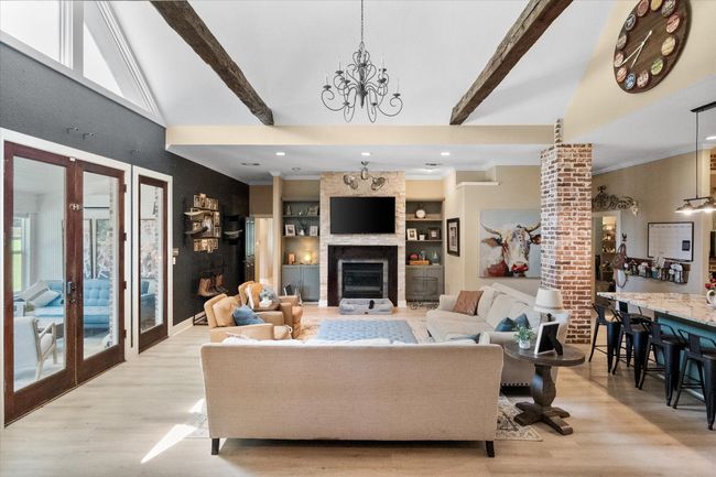 Living room featuring wood finished floors, french doors, a chandelier, a large fireplace, and ornamental molding | Image 4