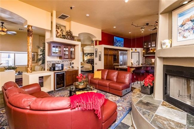 Living area featuring wine cooler, arched walkways, ceiling fan, a fireplace with raised hearth, and bar | Image 61