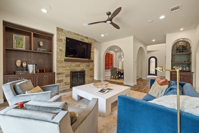 Living room with arched walkways, ceiling fan, wood finished floors, a stone fireplace, and built in shelves | Image 9