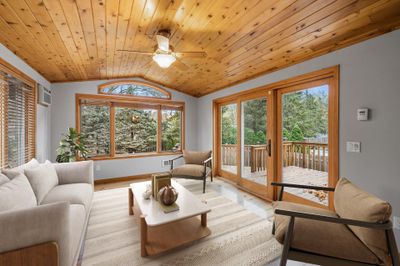 The stunning four-season porch features a beautiful cedar plank ceiling, durable laminate floors, and large windows that flood the space with natural light. With convenient deck access, this room is perfect for year-round enjoyment! | Image 1