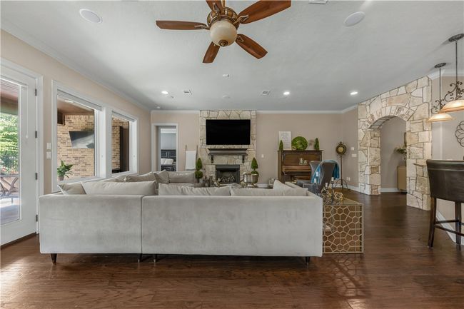 Living area with a fireplace, ceiling fan, ornamental molding, arched walkways, and dark wood-type flooring | Image 12