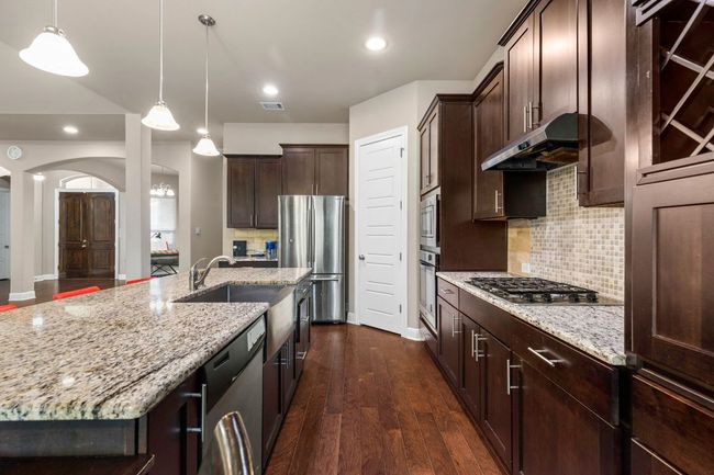 Kitchen with stainless steel appliances, under cabinet range hood, light stone countertops, dark wood-style flooring, and decorative backsplash | Image 13