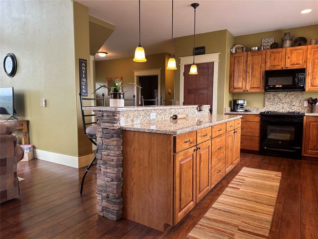 Kitchen featuring black appliances, a kitchen breakfast bar, dark wood-style flooring, and a center island | Image 4