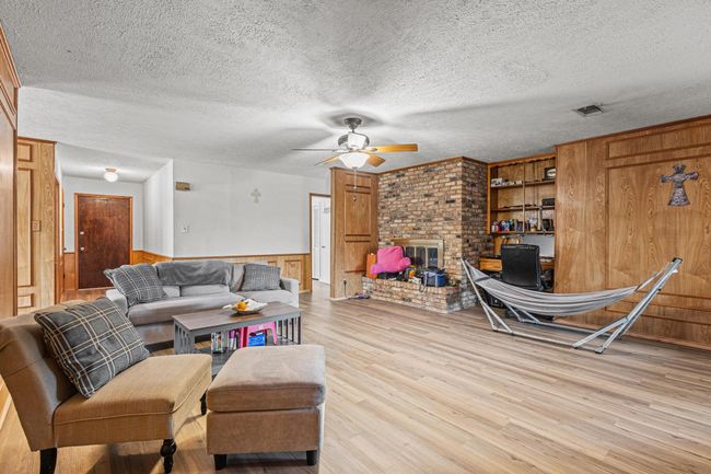 Living area featuring ceiling fan, wood finished floors, a fireplace, wooden walls, and a wainscoted wall | Image 15