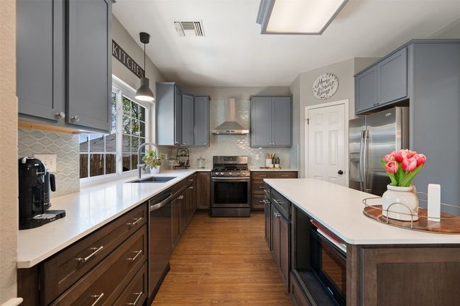 Kitchen with visible vents, wood finished floors, wall chimney exhaust hood, stainless steel appliances, and a sink | Image 13