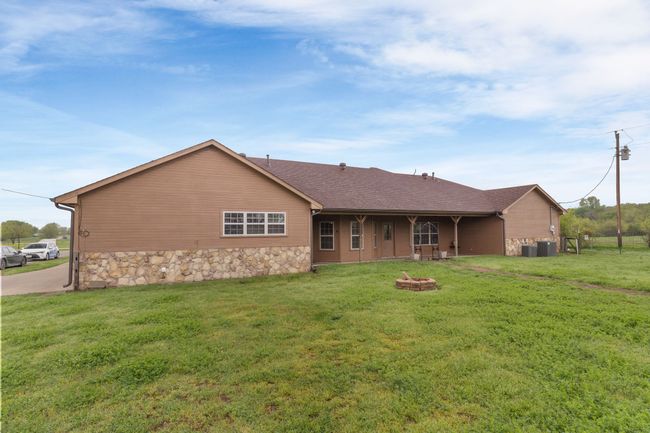 Rear view of house with a yard, roof with shingles, stone siding, and an outdoor fire pit | Image 5