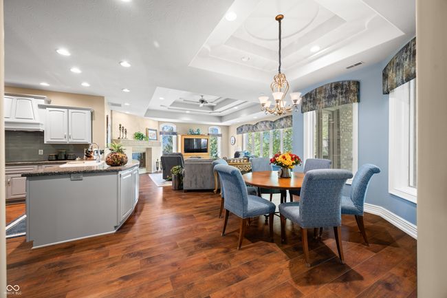 dining space with dark wood finished floors, a glass covered fireplace, a tray ceiling, visible vents, and ceiling fan with notable chandelier | Image 23