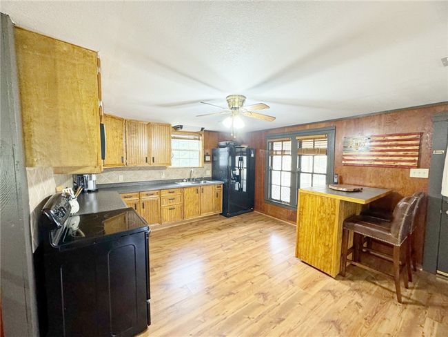 Kitchen with a sink, light wood-type flooring, a ceiling fan, black appliances, and backsplash | Image 5