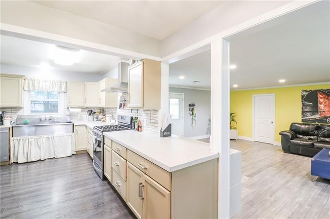 Kitchen featuring stainless steel appliances, wall chimney exhaust hood, light countertops, decorative backsplash, and recessed lighting | Image 5
