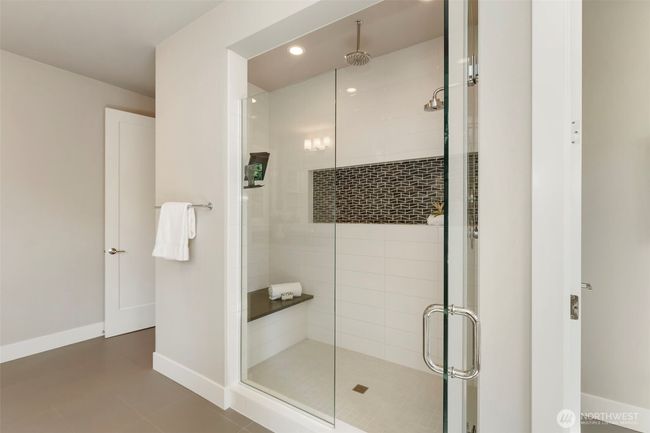 This alternate view of the primary bath highlights the spacious walk-in shower, complete with a built-in bench, dual showerheads—including a rain option—and stylish mosaic tile accent. It’s a luxurious, spa-like escape designed with both comfort and elegance in mind. | Image 31