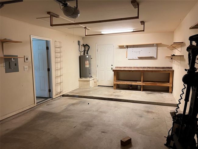Garage with a workshop area, water heater, a garage door opener, and electric panel | Image 12