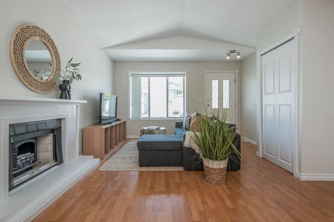 Living room with lofted ceiling, a fireplace with raised hearth, baseboards, an inviting chandelier, and wood finished floors | Image 5