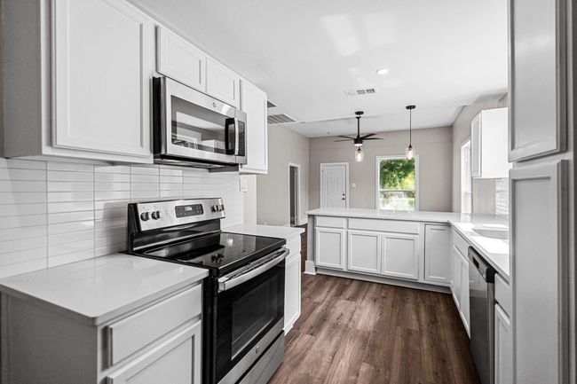 Kitchen with appliances with stainless steel finishes, a peninsula, ceiling fan, dark wood-style flooring, and backsplash | Image 6